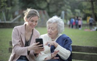 dame âgée en compagnie d'une jeune femme qui lui montre son téléphone